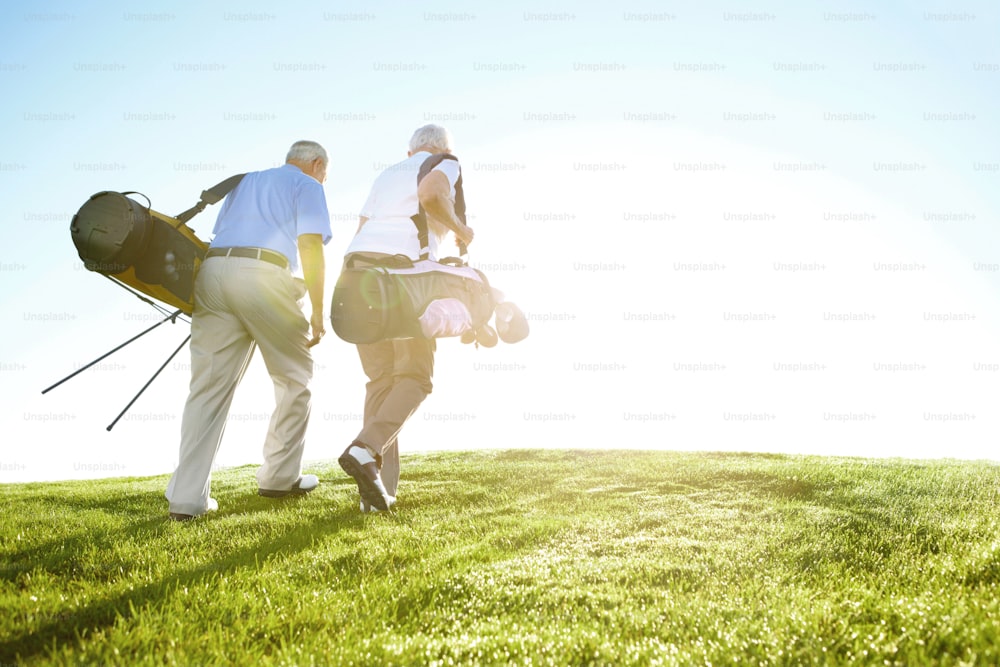 "Una pareja de ancianos cargando sus bolsas de golf y caminando por la calle contra un cielo azul y soleado"