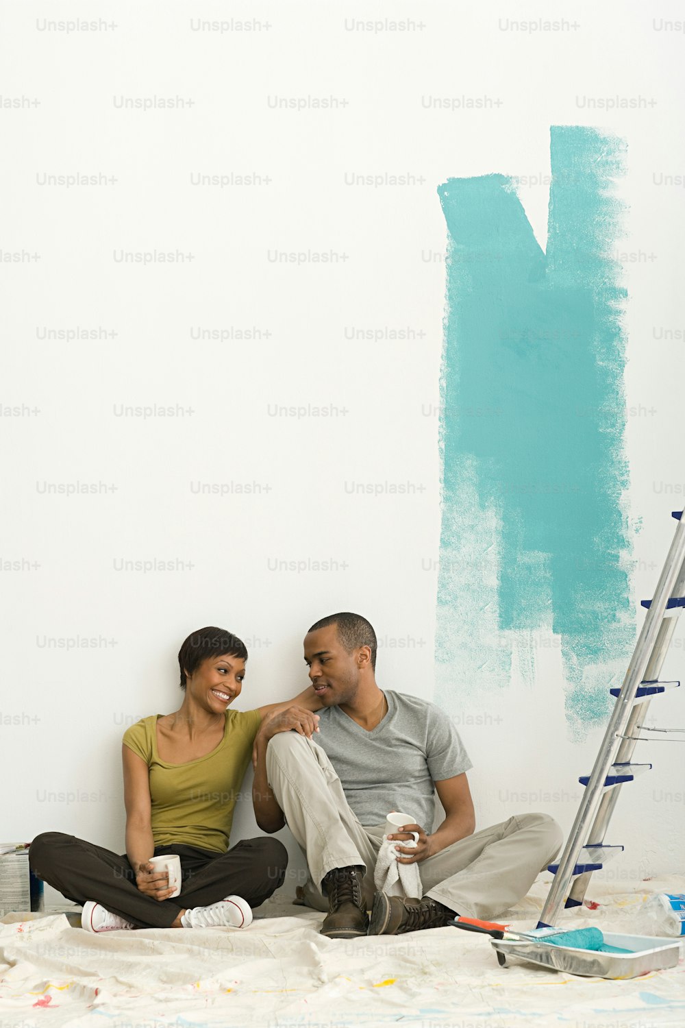 a man and a woman sitting on the floor in front of a wall with paint