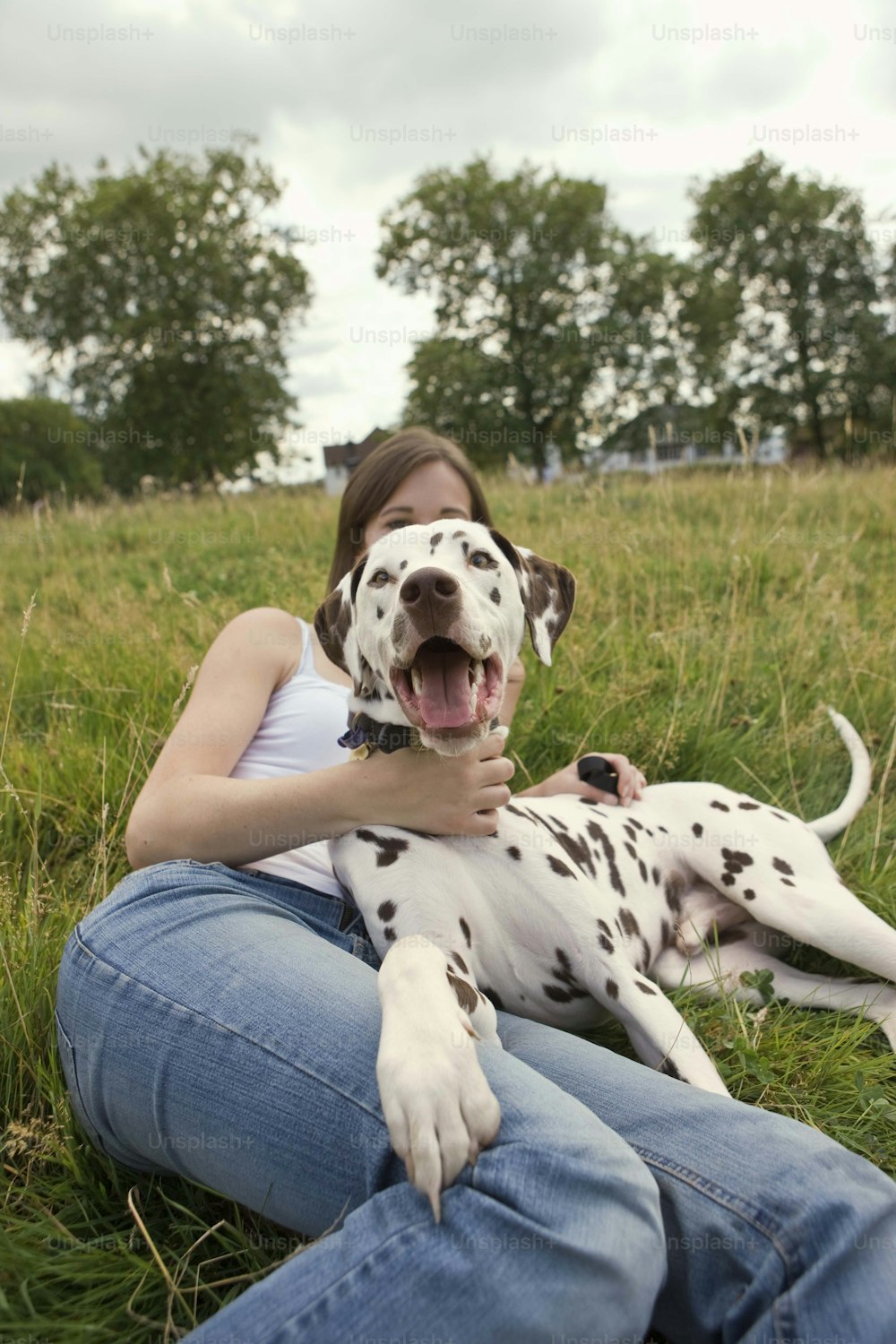a woman sitting in the grass with a dalmatian dog