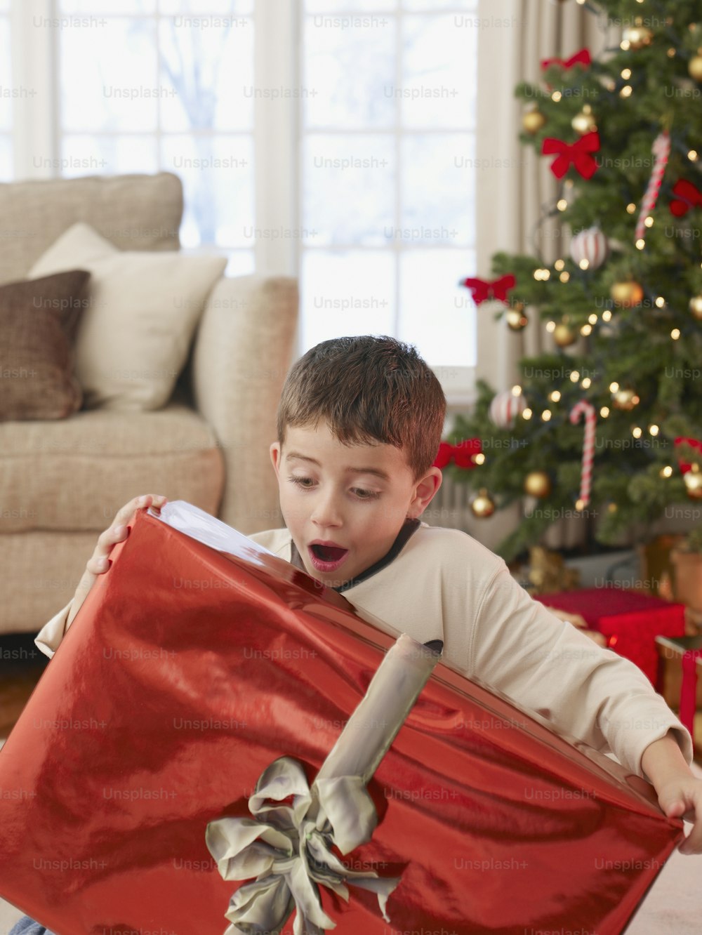 Ein kleiner Junge öffnet ein Weihnachtsgeschenk vor einem Weihnachtsbaum