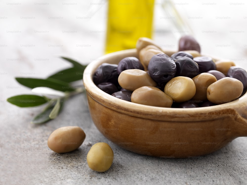un bol en bois rempli d’olives à côté d’une bouteille d’huile d’olive