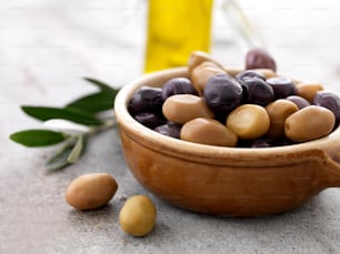 a wooden bowl filled with olives next to a bottle of olive oil