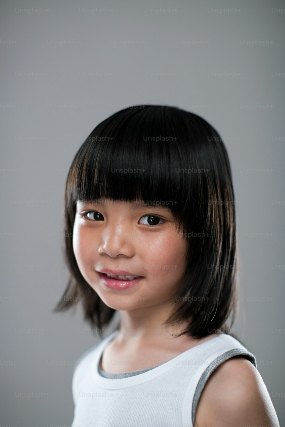 a young girl with black hair wearing a white tank top