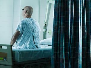 Un uomo in camice d'ospedale seduto su un letto d'ospedale