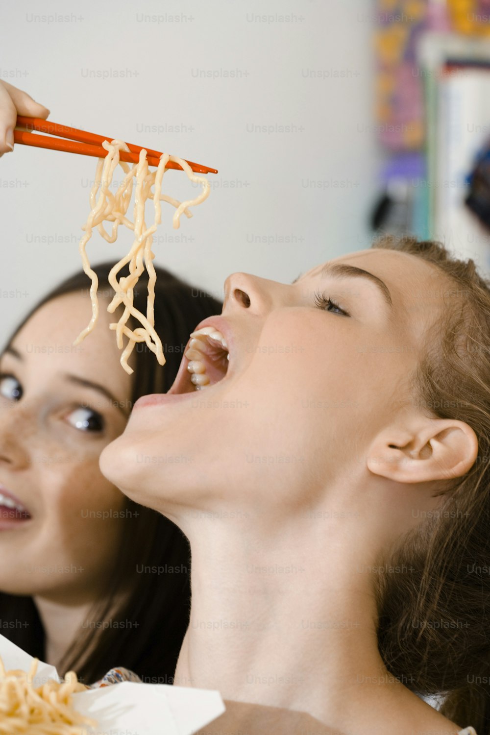 Una mujer comiendo fideos con palillos mientras otra mujer mira
