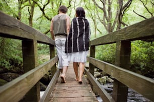 a man and a woman walking across a wooden bridge