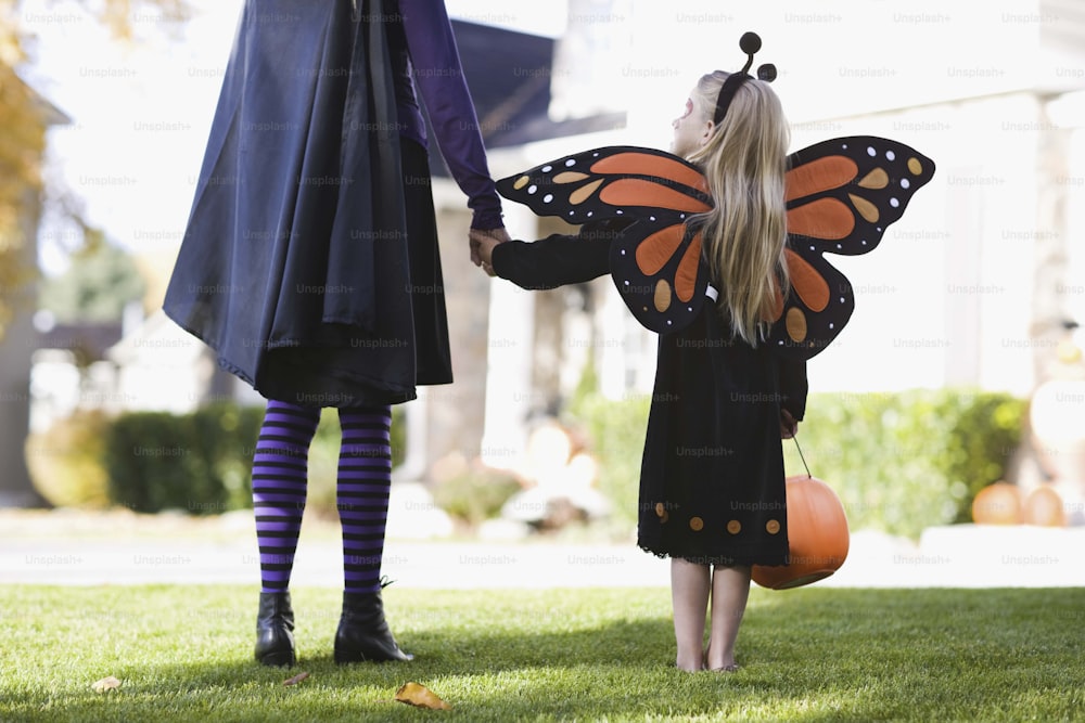 uma menina vestida como uma borboleta de mãos dadas com uma mulher em um vestido preto