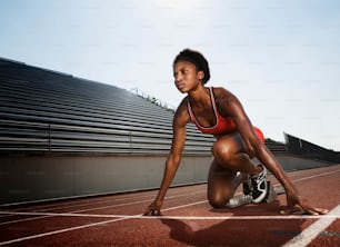 Une femme en soutien-gorge de sport rouge s’accroupit sur une piste