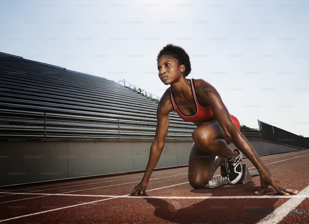 a woman in a red sports bra crouches on a track