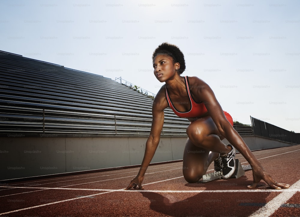 赤いスポーツブラを着た女性がトラックにしゃがむ