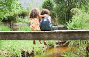 two children sitting on a wooden bridge over a stream