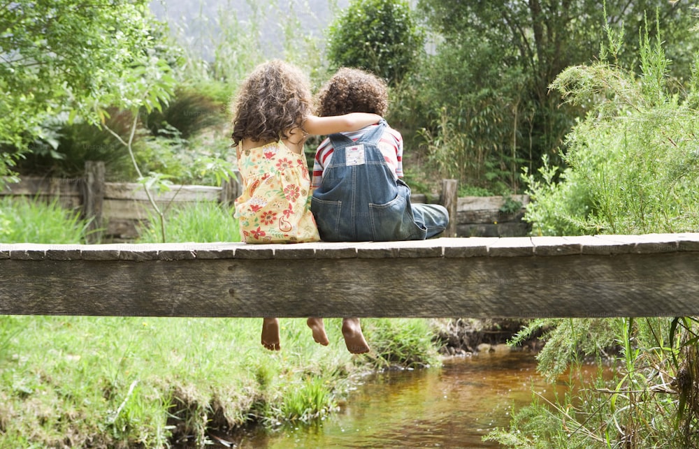 개울 위의 나무 다리에 앉아 있는 두 아이