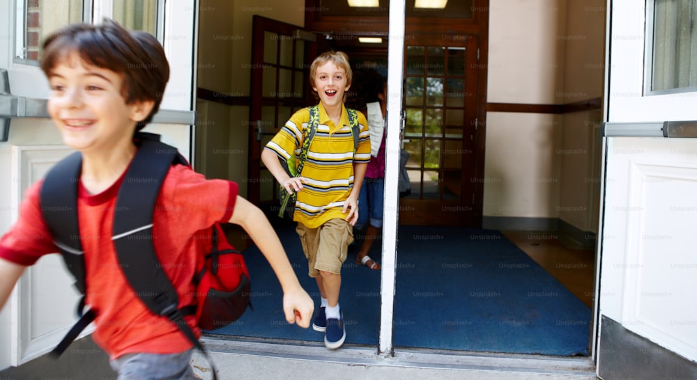 Jovens estudantes do sexo masculino saem correndo pela porta da frente de sua escola após o toque do sino
