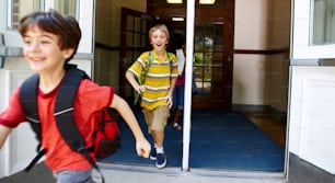 Jóvenes estudiantes varones salen corriendo por la puerta principal de su escuela después de que suene la campana