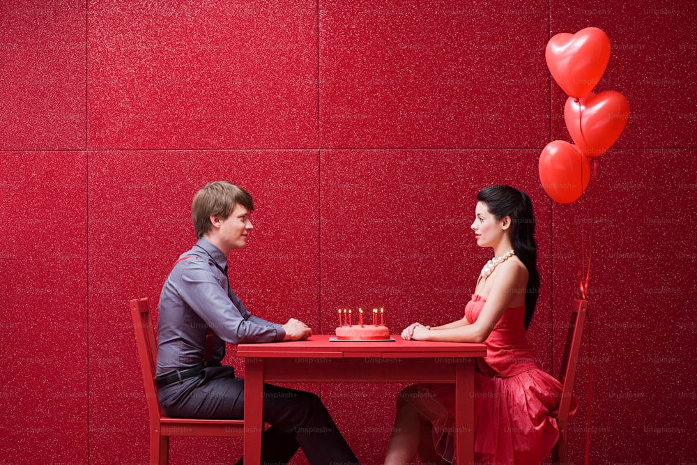 a man and woman sitting at a table with red balloons