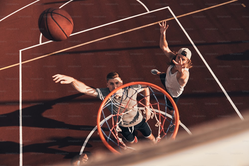 Vista superior do jovem em roupas esportivas marcando um slam dunk enquanto joga basquete ao ar livre