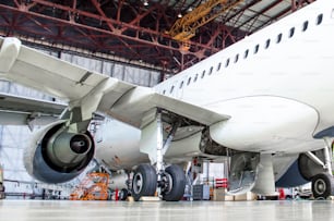 Aeronaves de pasajeros en mantenimiento de reparación de motores y fuselaje en hangar de aeropuertos. Vista trasera, bajo el ala