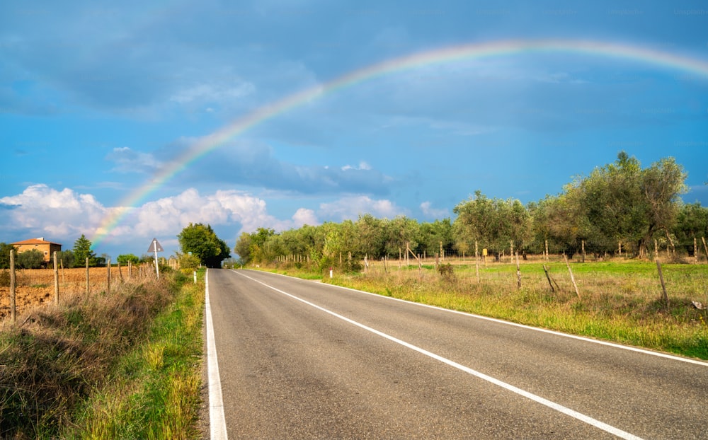 Arco iris sobre la carretera de la carretera del campo y el paisaje agrícola en la Toscana, Italia.