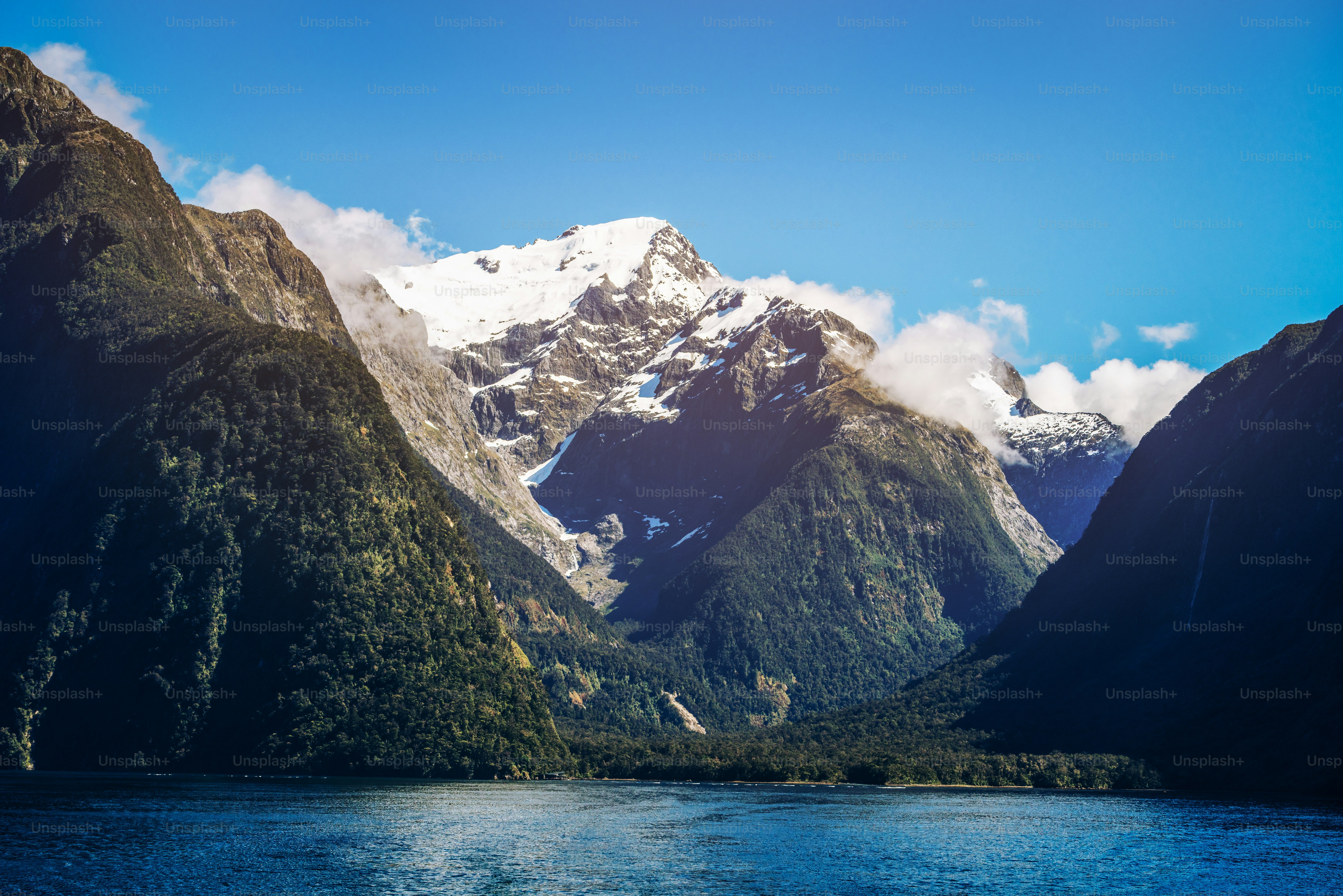 Lake and mountain landscape with snow capped peak under summer sunlight in blue sky background. Shot in Milford Sound, Fiordland National Park, South Island of New Zealand.
