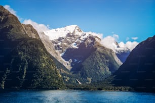 Paisagem do lago e da montanha com pico coberto de neve sob a luz solar do verão no fundo azul do céu. Filmado em Milford Sound, Parque Nacional de Fiordland, Ilha Sul da Nova Zelândia.