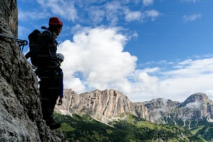 two young mountain climbers in silhouette on a steep and exposed climb in the Dolomites of Alta Badia in Italy with a great view of the Val Gardena behind them