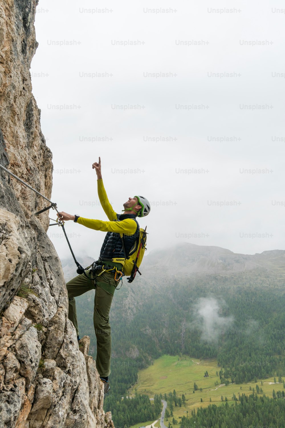 young attractive male mountain climber on a steep and exposed Via Ferrata in Alta Badia in the South Tyrol in the Italian Dolomites pointing to the summit