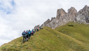 A large group of climbers and two mountain guides hiking towards the start of a climb in the Dolomites of Alta Badia in northern Italy