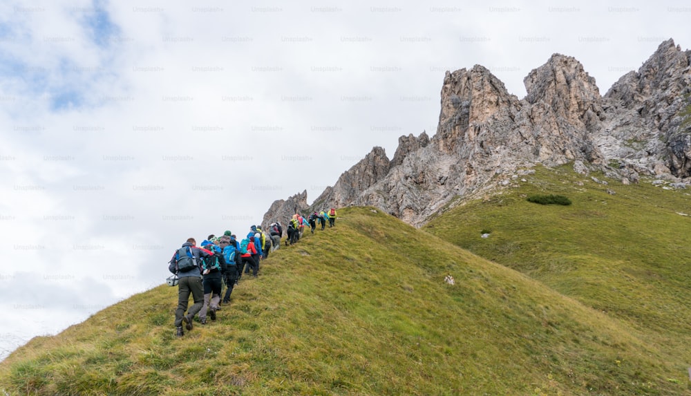 A large group of climbers and two mountain guides hiking towards the start of a climb in the Dolomites of Alta Badia in northern Italy