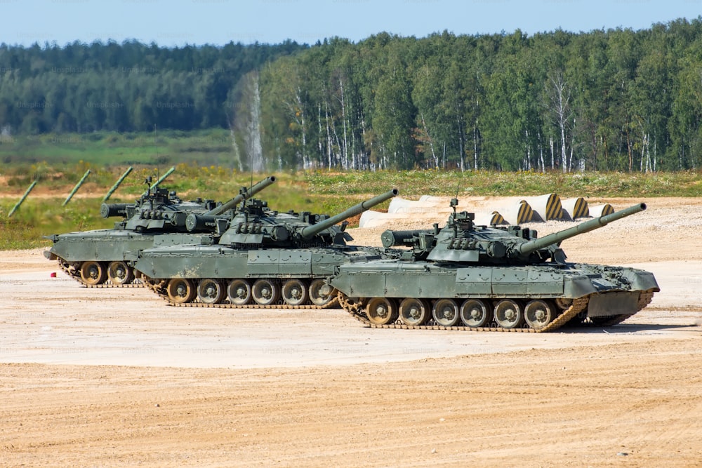 Three military tanks stand on the field with muzzles raised in the sky
