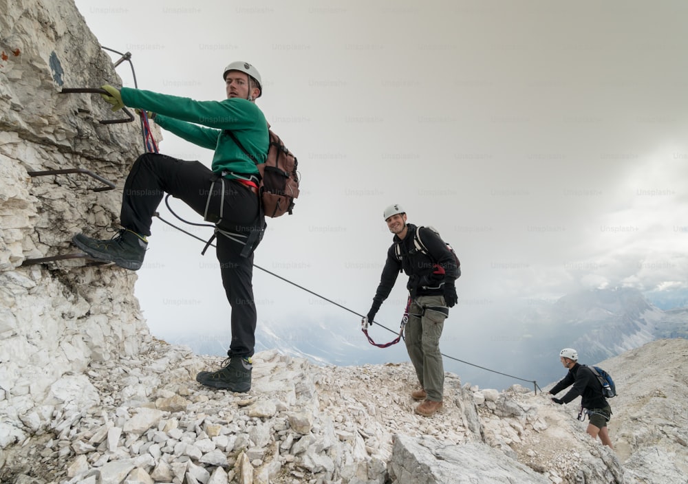 group of young mountain climbers on a steep Via Ferrata with a grandiose view of the Italian Dolomites in Alta Badia behind them