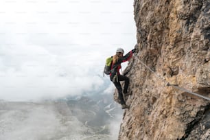 jovem estudante universitária atraente em uma rocha vertical e exposta sobe uma Via Ferrata em Alta Badia, no sul do Tirol
