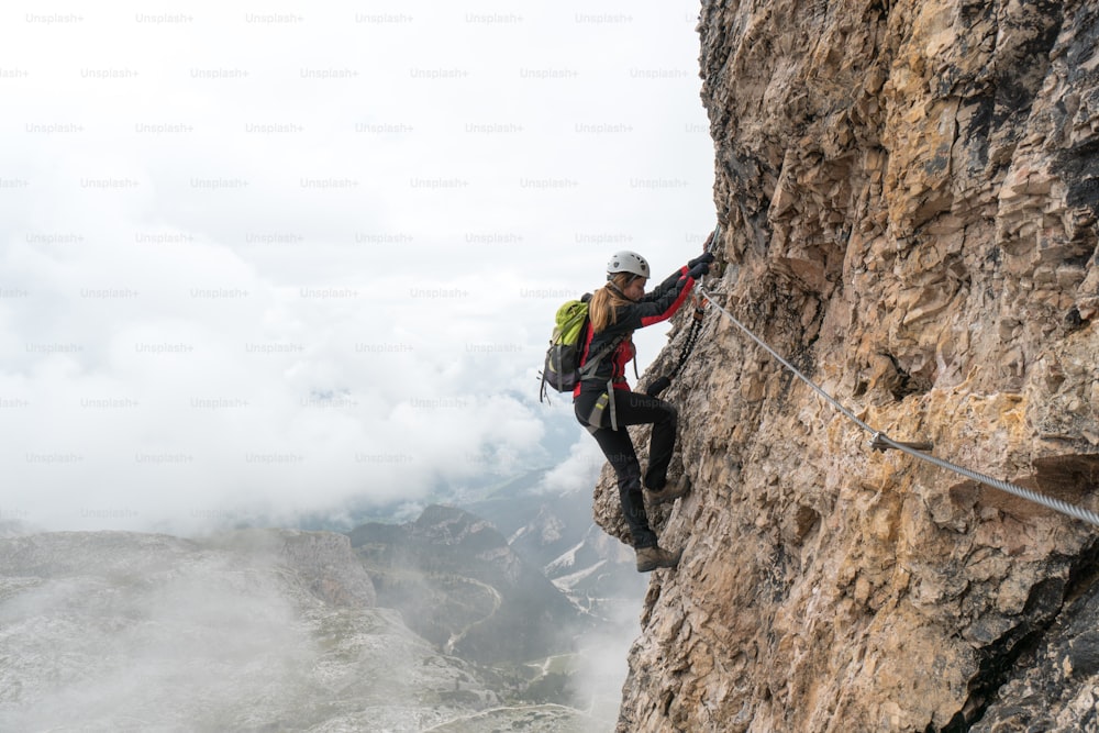 giovane attraente studentessa universitaria su una parete rocciosa verticale ed esposta sale una via ferrata in Alta Badia in Alto Adige
