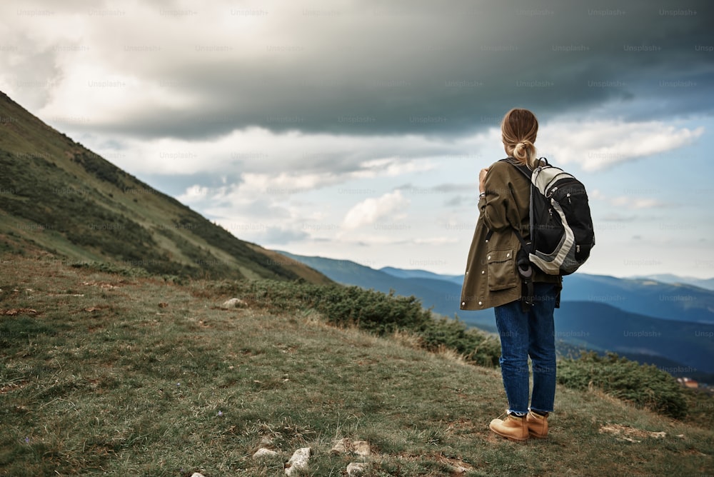 Peaceful place. Calm young woman carrying her big heavy backpack and peacefully looking at the beautiful landscape