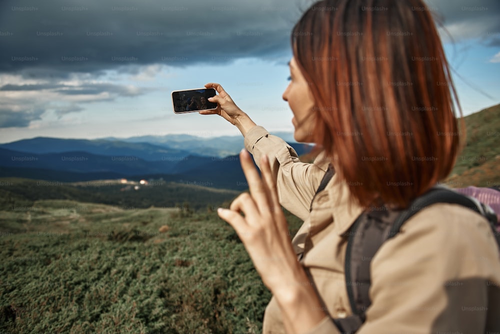 Selfie alone. Cheerful young traveler being in the mountains and holding modern smartphone while taking selfies alone