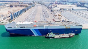 Aerial view Vehicle carrier vessel cruising at car park in sea port or manufacture waiting for shipping export to worldwide.