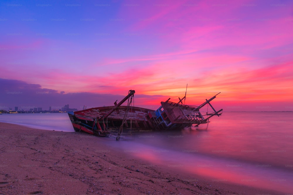 Longa exposição o antigo naufrágio ter abandonado na praia com céu crepuscular colorido na hora do pôr do sol