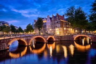 Vista nocturna del paisaje urbano de Amterdam con el canal, el puente y las casas medievales en el crepúsculo de la tarde iluminado. Ámsterdam, Países Bajos