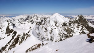 Ein männlicher Backcountry-Skifahrer erklimmt und wandert einen langen, exponierten schmalen Schneegrat in den Schweizer Alpen auf seinem Weg zu einem hohen Berggipfel in der Silvretta.