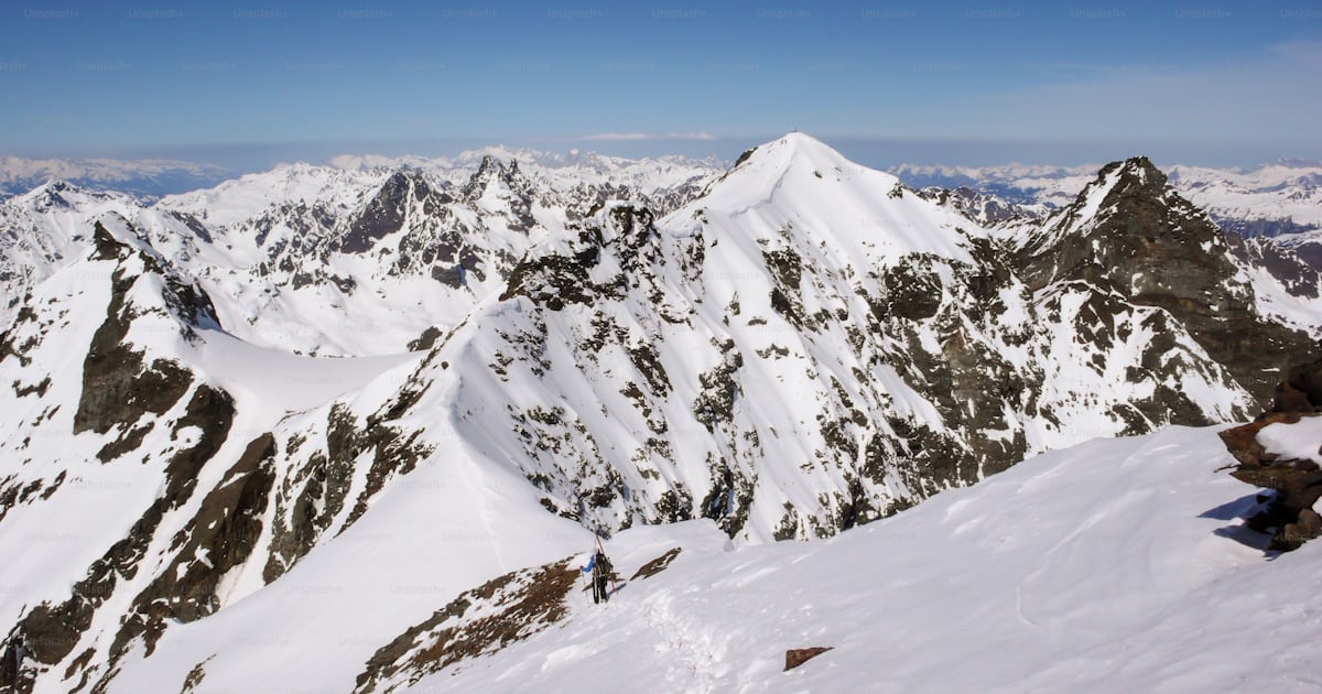 A male backcountry skier climbs and hikes a long exposed narrow snow ...
