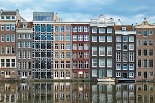 Row of typical houses and boat on Amsterdam canal Damrak with reflection. Amsterdam, Netherlands