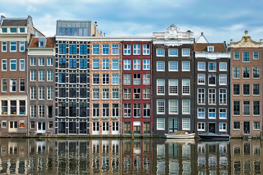 Hilera de casas típicas y barco en el canal Damrak de Ámsterdam con reflexión. Ámsterdam, Países Bajos