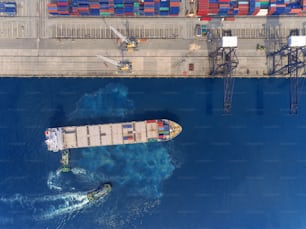 Aerial top view Tug boat drag container ship at sea port to crane bridge for load container, logistics import export, shipping or transportation concept background.