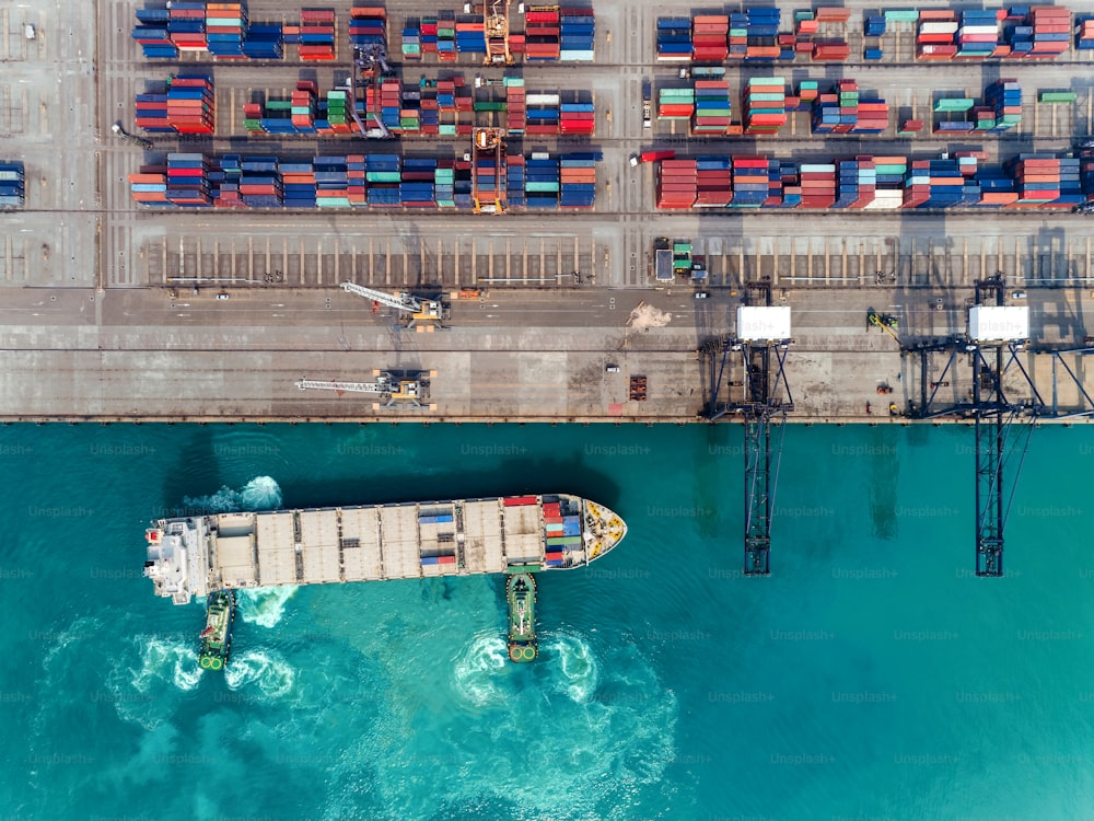 Rimorchiatore con vista aerea dall'alto che trascina la nave portacontainer al porto marittimo al ponte della gru per il contenitore di carico, l'importazione di logistica, l'esportazione, il trasporto o il concetto di trasporto.
