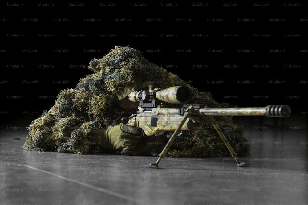 The sniper in disguise lies with a sniper rifle and aims at the telescopic sight. Mixed media