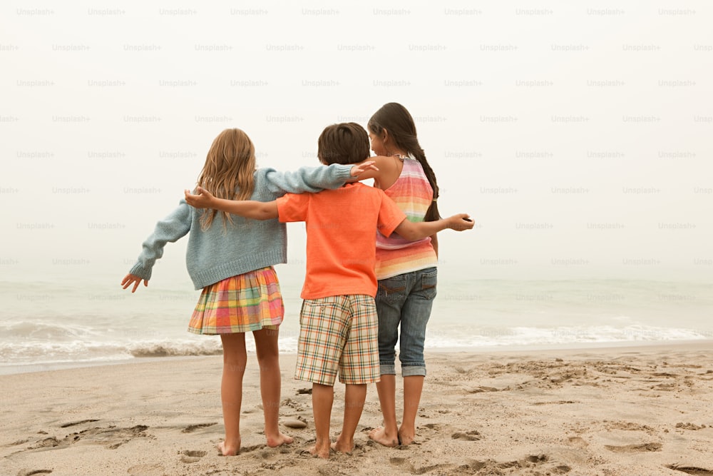 a group of young children standing on top of a sandy beach