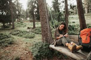 This is important. Portrait of beautiful young lady writing in notebook and smiling. Trees and green plants on background