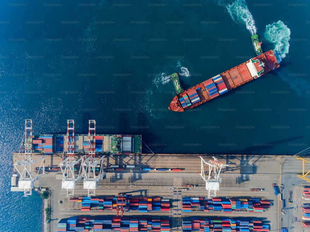 Aerial top view Tugboat draging container ship at sea port to working crane bridge loading container for logistics import export, shipping or transportation concept background.