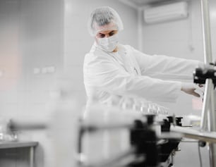 Picture of young man in sterile clothes controlling production line of cosmetic products. Standing in bright room and using control board..