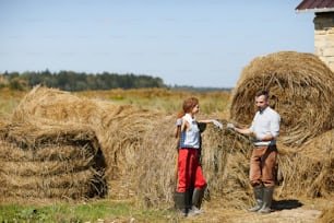 Male and female farmers looking at hay sample while working outdoors by stack