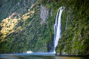 Ein Sightseeing-Boot mit Touristen nähert sich dem großen Wasserfall im Milford Sound. Wunderschöne malerische Kreuzfahrt durch den Fiordland National Park auf der Südinsel Neuseelands.